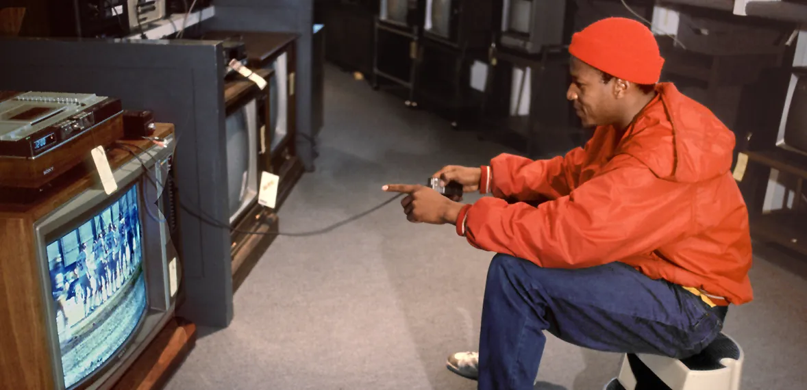 Customer in a red jacket photographing a bank of CRT televisions in an electronics showroom